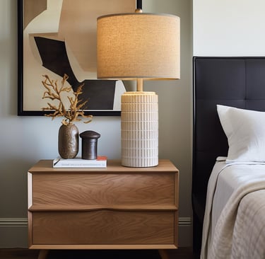 Modern bedroom nightstand with a ceramic table lamp, decorative vase, and abstract wall art.