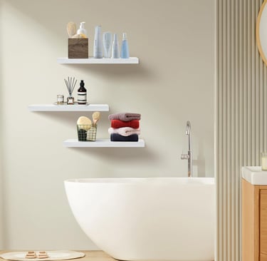 White floating wall shelves in a bathroom above a bathtub holding towels and toiletries.