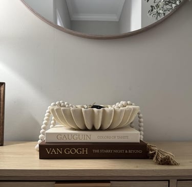 Scalloped decorative bowl on stacked art books with wood beads on a console table.
