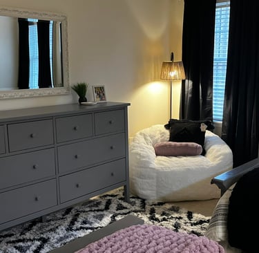 Modern bedroom featuring a gray dresser, white shag bean bag chair, and black curtains.