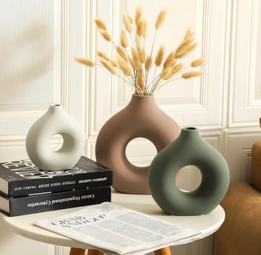 Three modern ceramic donut vases in white, brown, and green with dried pampas grass on a side table.