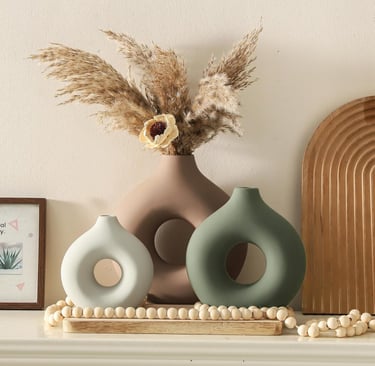 Modern donut-shaped ceramic vases in neutral tones with pampas grass on a mantle decor display.