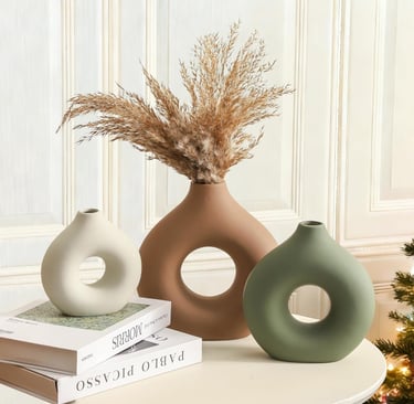 Set of three modern donut ceramic vases in cream, terracotta, and green with dried pampas grass decor.