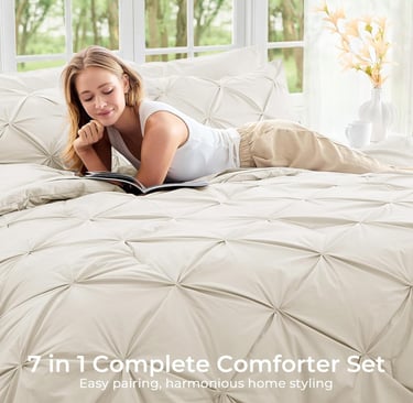 Woman relaxing on a beige pinch pleat comforter set while reading a book in a bright bedroom.