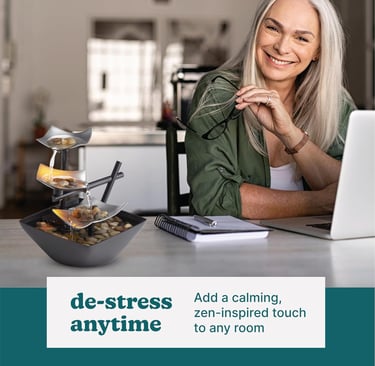 A smiling woman sitting at a desk next to a tiered indoor desktop water fountain for home office relaxation.