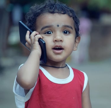 Young Indian toddler with curly hair holding a smartphone to his ear making a phone call.