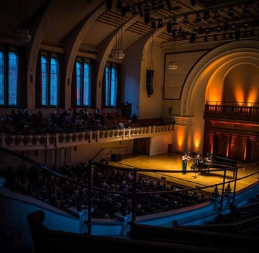 Violinist and pianist perform a classical music concert for an audience in a historic grand hall.