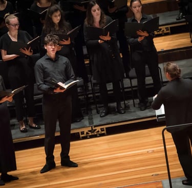 Professional choir singers in black formal attire performing a choral concert with a conductor on stage.
