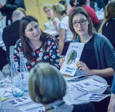 Professional woman holding a Mind and Body case study booklet while networking at a corporate event workshop.