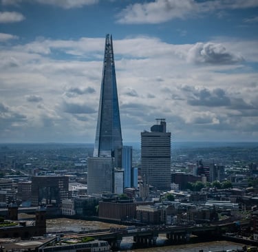 Aerial view of The Shard skyscraper towering over the London city skyline under a cloudy blue sky.