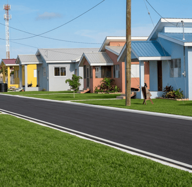 A row of modern, colorful suburban houses with paved roads and green lawns in a new residential development.