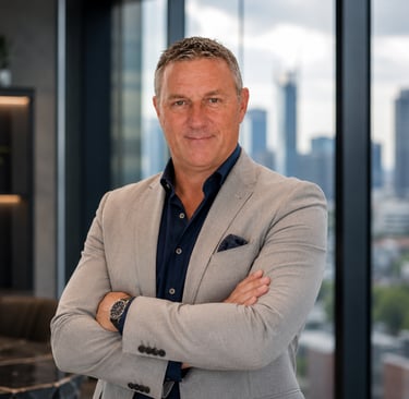 Professional male executive in a grey blazer posing in a modern office with a city skyline view.