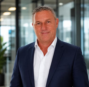 Professional portrait of a middle-aged male executive in a navy blue blazer and white shirt in a modern office.