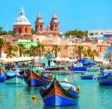 Colorful traditional Luzzu boats floating in Marsaxlokk harbor with the historic parish church in Malta.