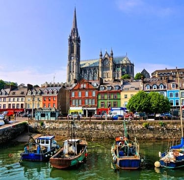 Fishing boats in Cobh harbor with colorful houses and St. Colman's Cathedral in Ireland.