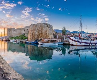 Kyrenia Harbour in Northern Cyprus featuring the historic castle and sailboats at sunset.