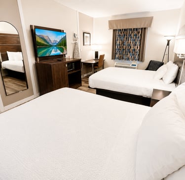 Modern hotel room with two queen beds, a flat-screen TV, desk, and full-length mirror.