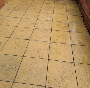 After yellow patio paving slabs next to a red brick wall, showing the need for patio cleaning.
