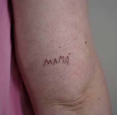 Tatuaje fineline en Madrid con lettering MAMÁ en mayúsculas trazo fino en el brazo
