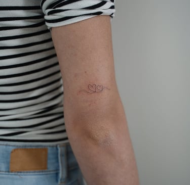 Tatuaje fineline en Madrid de dos corazones pequeños unidos por línea continua en el brazo
