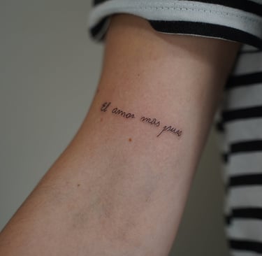 Tatuaje fineline en Madrid con frase el amor más puro en cursiva fina en el antebrazo