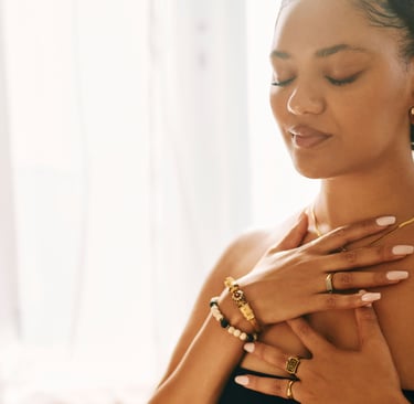 Uma mulher serena, usando joias de ouro, pratica meditação mindfulness com as mãos sobre o peito.