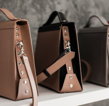 Collection of stylish leather satchel handbags with metal stud details displayed on a shelf.