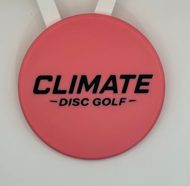 A pink Climate Disc Golf mini marker disc with black embossed lettering on a white background.