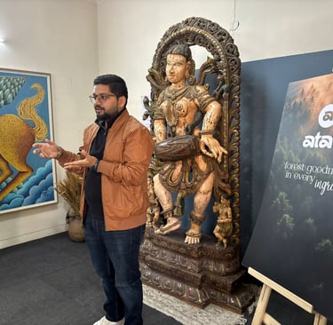 A man presenting next to an ancient Indian wooden sculpture and Atavi forest brand signage in an art gallery.
