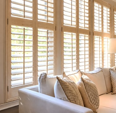 Shutters filtering direct midday light onto a plaster wall.