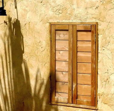 Slim timber window with shutters set into a thick Mediterranean stone wall.