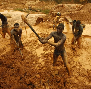 Artisanal gold miners using pickaxes and shovels to excavate muddy soil at an open-pit mine site.