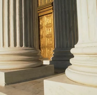White marble fluted columns of a neoclassical building leading to an ornate golden door.