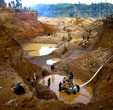 Miners working at an artisanal open-pit gold mine in a deep muddy excavation site with pumps.