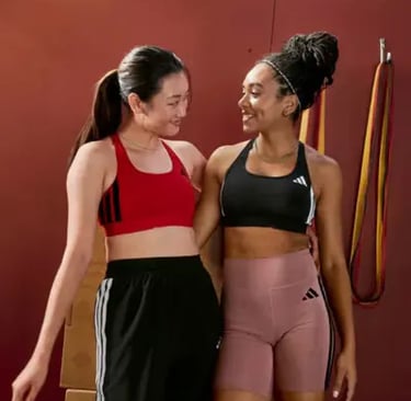 Two women smiling in Adidas sports bras and gym wear during a workout session.