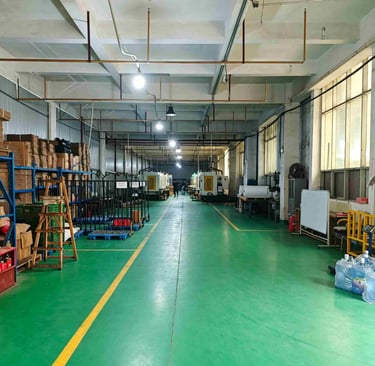 Industrial manufacturing facility with green floors, injection molding machines, and organized storage shelves.