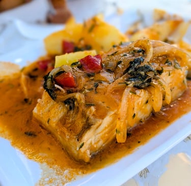 Close-up of cod cooked in a tomato, onion, and pepper sauce.