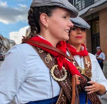 Close-up of two women in traditional Spanish festival attire with papusas, red scarves, and leather harnesses.