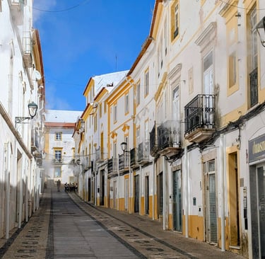 Narrow street in Elvas lined with whitewashed Alentejo buildings with yellow trim under a blue sky.