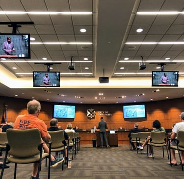 Photo from the back of city council with someone in the center talking at the podium