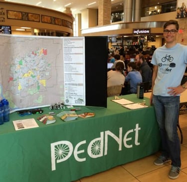 Lawrence posing by a table reading "PedNet" with a map trifold