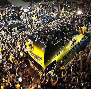 AEK Athen Fan im Stadion jubelt leidenschaftlich während eines Spiels, Fahnen wehend, Gesänge schallend, in voller Fan-Ausrüs