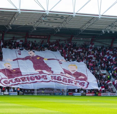 Innenansicht des Tynecastle Park in Edinburgh: dicht gefüllte Tribünen mit jubelnden Fans, rot-weißen Vereinsfarben, klar erk