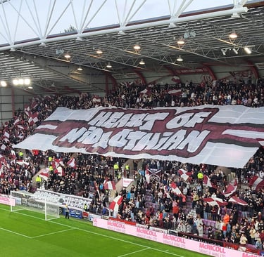Innenansicht des Tynecastle Park in Edinburgh: dicht gefüllte Tribünen mit jubelnden Fans, rot-weißen Vereinsfarben, klar erk