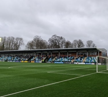 Innenansicht des Park Hall Stadium in Oswestry – Blick auf Spielfeld, Tribünen und Flutlicht, Heimat der The New Saints zwisc