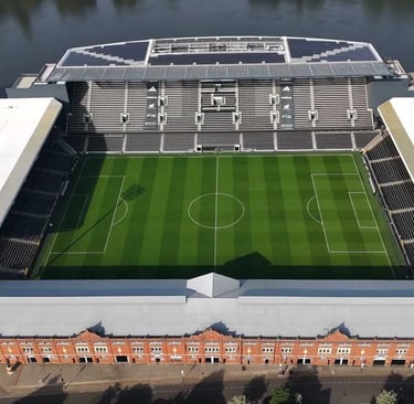 Vogelperspektive auf Craven Cottage, das Heimstadion von Fulham FC in London, mit Tribünen, Spielfeld und Themse im Hintergru
