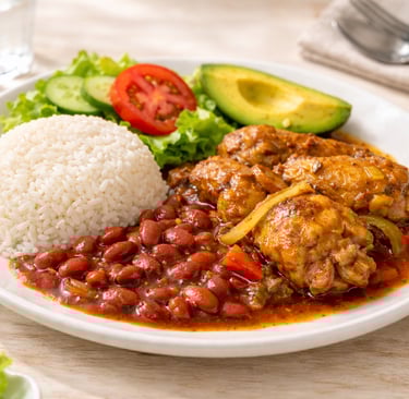 Dominican La Bandera national dish with white rice, red beans, stewed chicken, avocado, and fresh salad on a white plate
