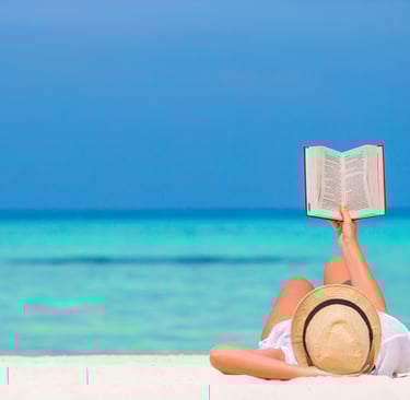 a woman reading a book while laying on the beach