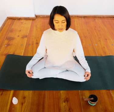 an asian woman sitted on a lotus position on a green matt, wearing all white