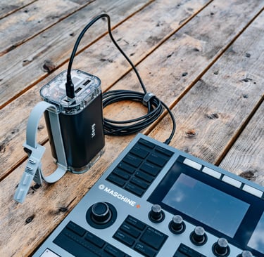 A professional music production setup featuring a Maschine+ controller and connected power source on a wooden table
